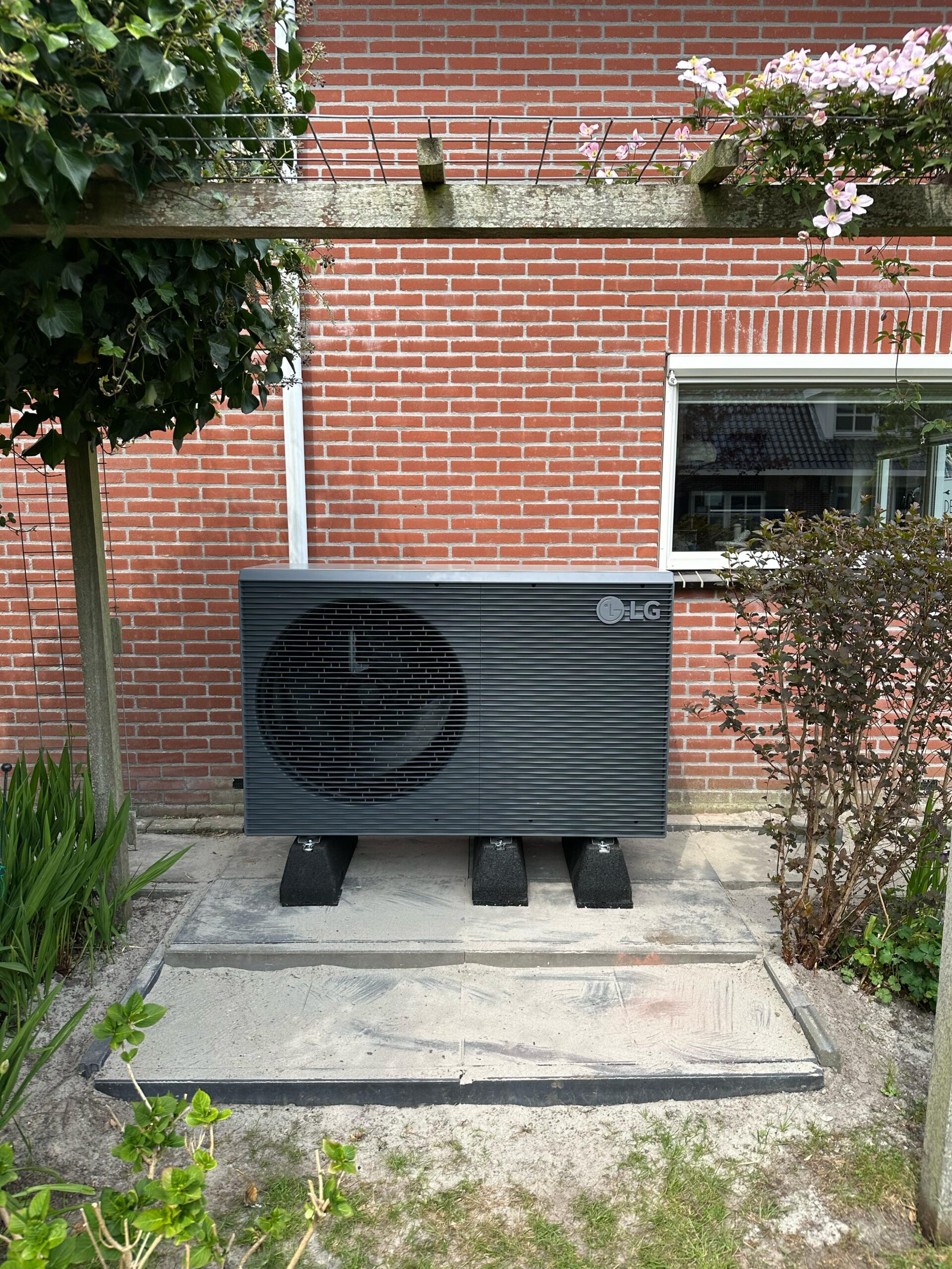 LG warmtepomp geïnstalleerd in de tuin tegen een gevel