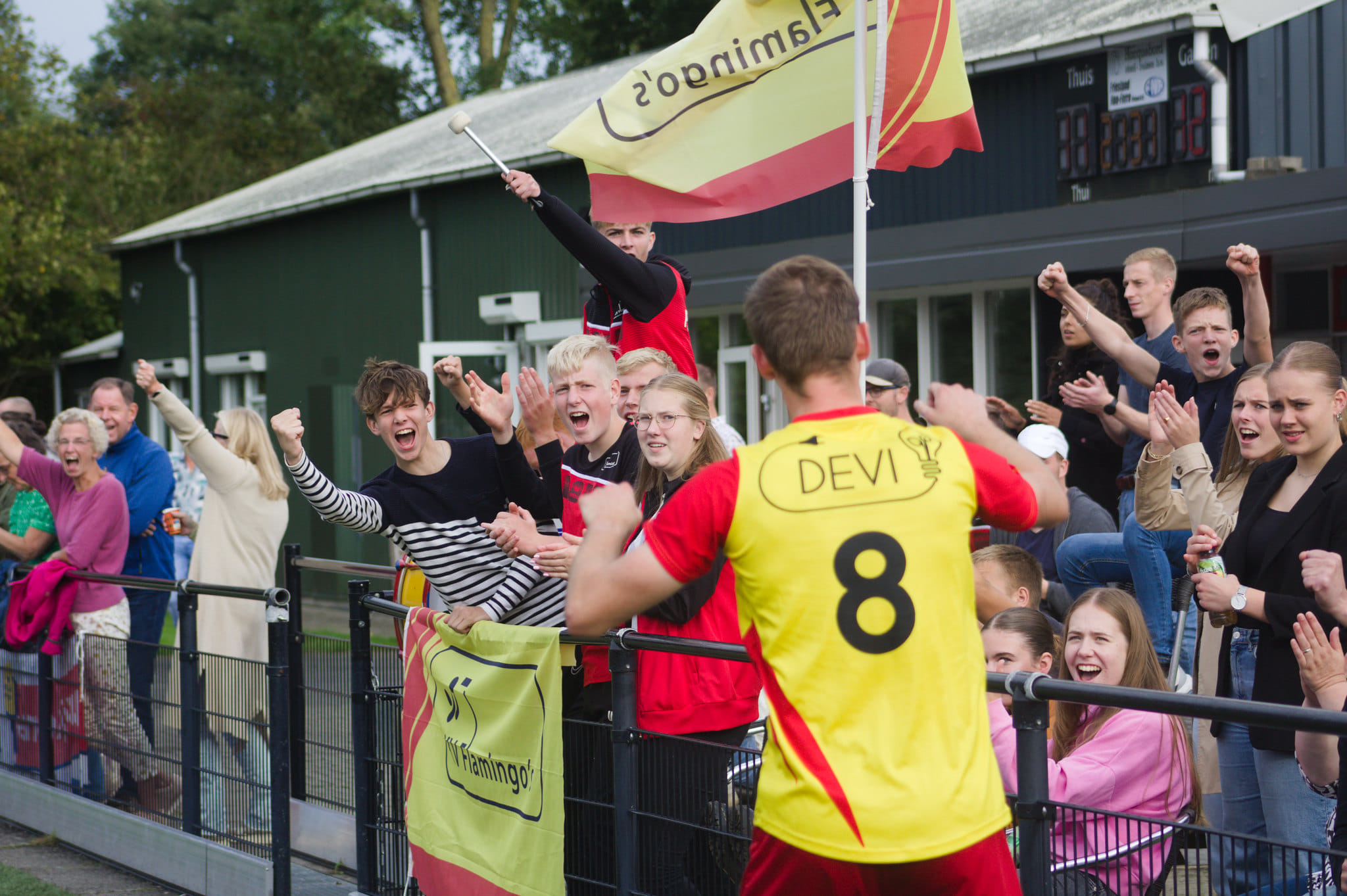 Supporters van KV Flamingo's juichen een speler met het DEVI-logo op zijn shirt toe